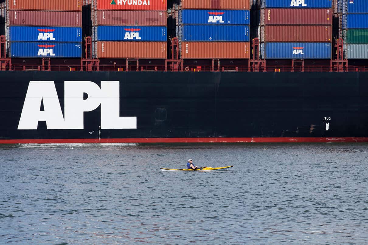 kayaker paddles in front of a cargo ship loaded with shipping containers