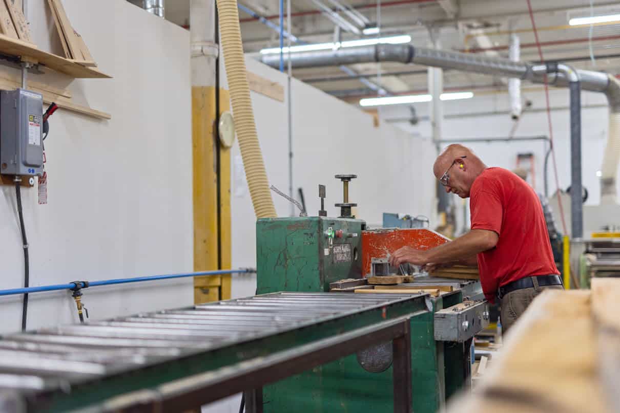a man works at industrial equipment in a warehouse making wooden paddles