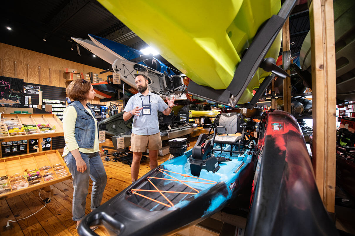 woman chats with a salesperson at the kayak shop about getting outfitted a beginner for kayak fishing
