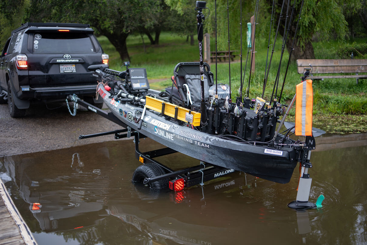 vehicle backs a fully rigged fishing kayak on a trailer into the water at the launch