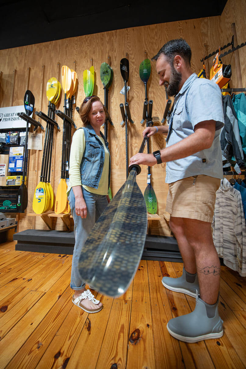 woman picks out a paddle for kayak fishing at a paddle shop