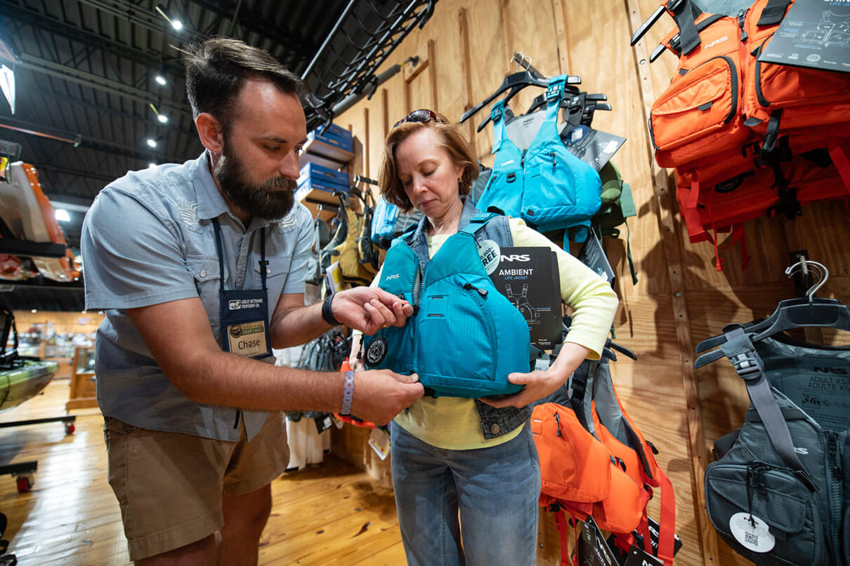 woman tries on a kayak fishing PFD at a paddle shop