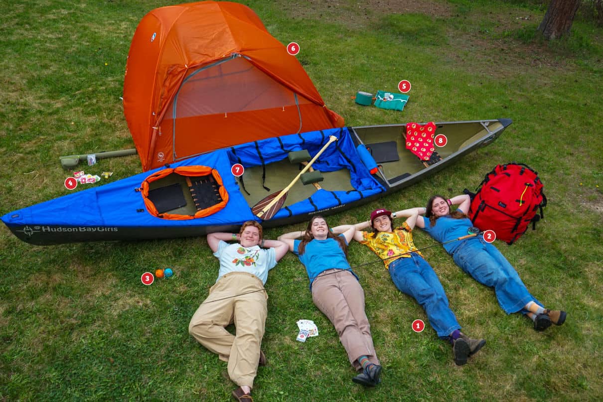 four members of the Hudson Bay Girls canoe expedition pose on a lawn with their gear for the trip