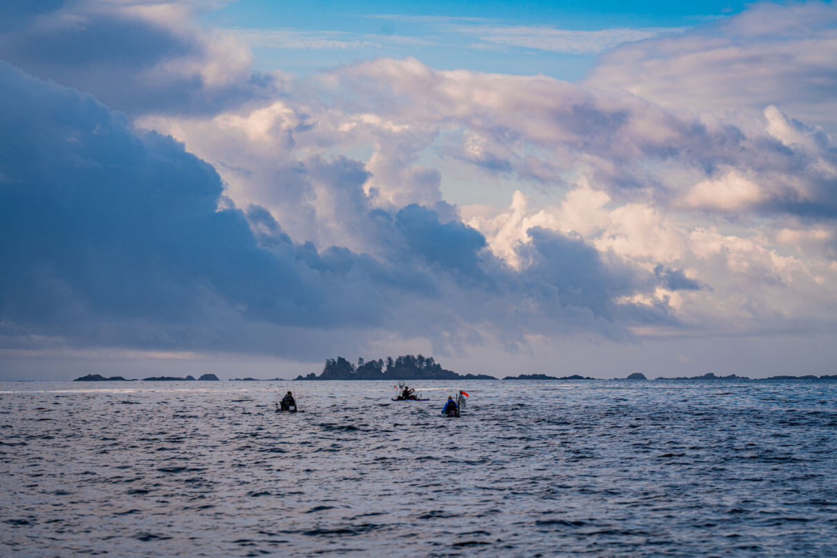 a group of kayak anglers on the Pacific with a small island behind them and dramatic clouds