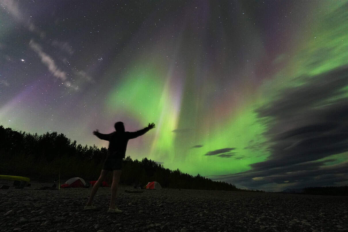 a person watches the northern lights along the Nahanni River