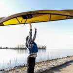 Best Lightweight Canoes For 2026 Woman tosses a lightweight Wenonah canoe overhead.