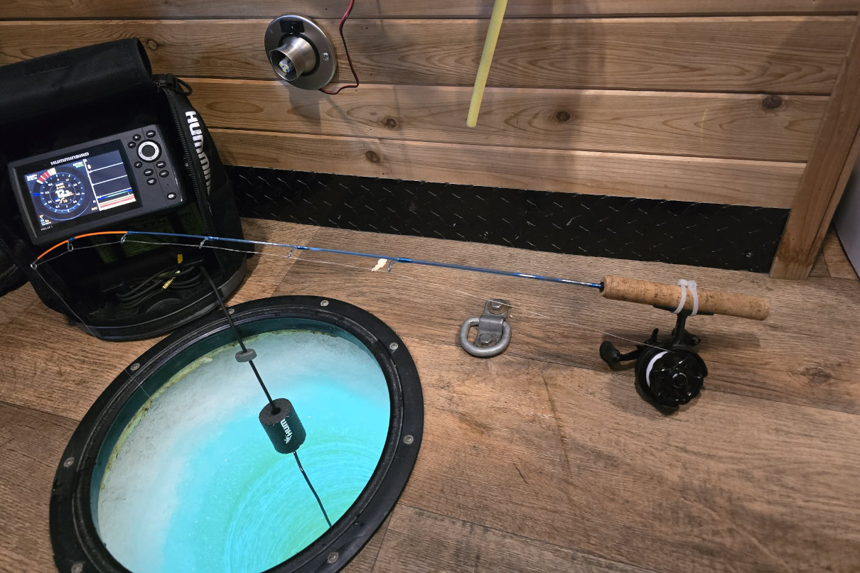Ice fishing rod set up in shelter over hole cut in ice.