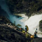 Greatest Whitewater Descents Of The Century (So Far) a group of whitewater kayakers stand on rocks overlooking the Kwanza River and its huge rapids