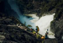 Greatest Whitewater Descents Of The Century (So Far) a group of whitewater kayakers stand on rocks overlooking the Kwanza River and its huge rapids
