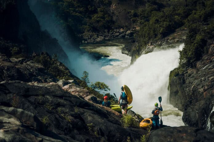 a group of whitewater kayakers stand on rocks overlooking the Kwanza River and its huge rapids