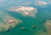 21 Industry Leaders On Paddlesports’ Most Pressing Issues two kayakers paddle around shallow turquoise watters with rocky islands just reaching the surface