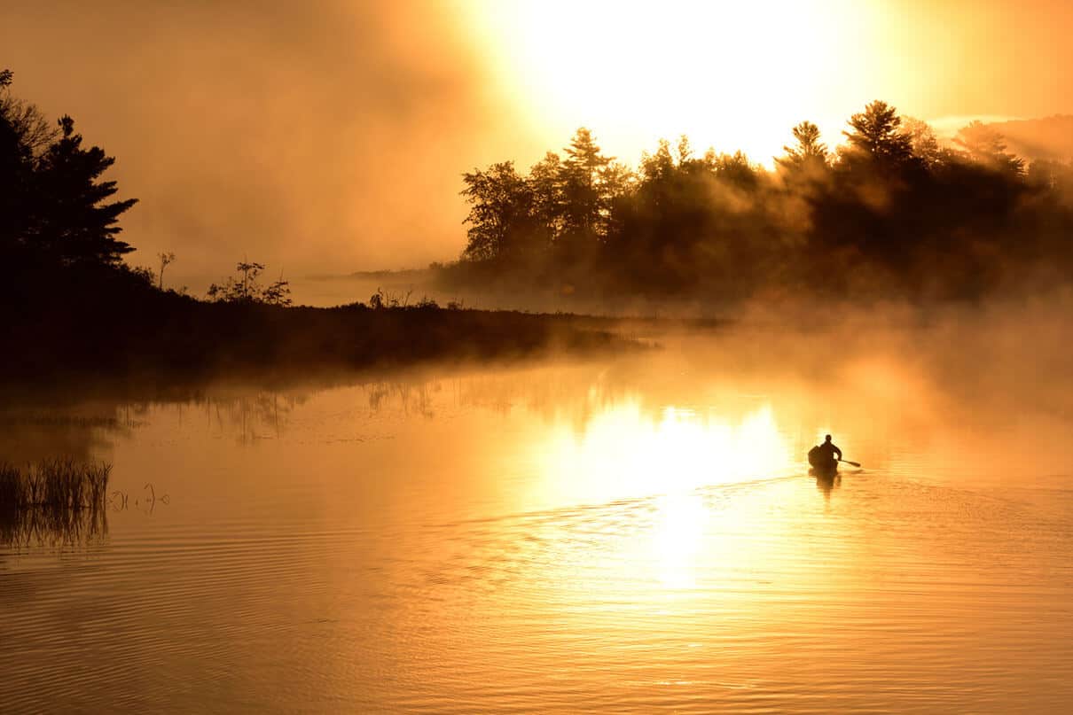 a person solo paddling a canoe while canoe tripping through misty waterways at dusk