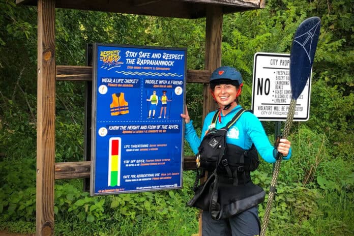 ACA Education Director and Smart Start co-author Kelsey Bracewell dressed in paddling gear and standing in front of paddling safety signage