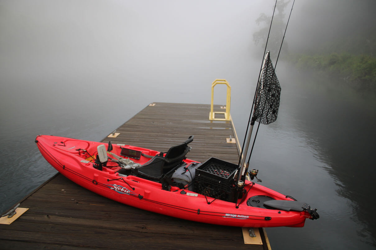 red fishing kayak on a dock by a misty lake