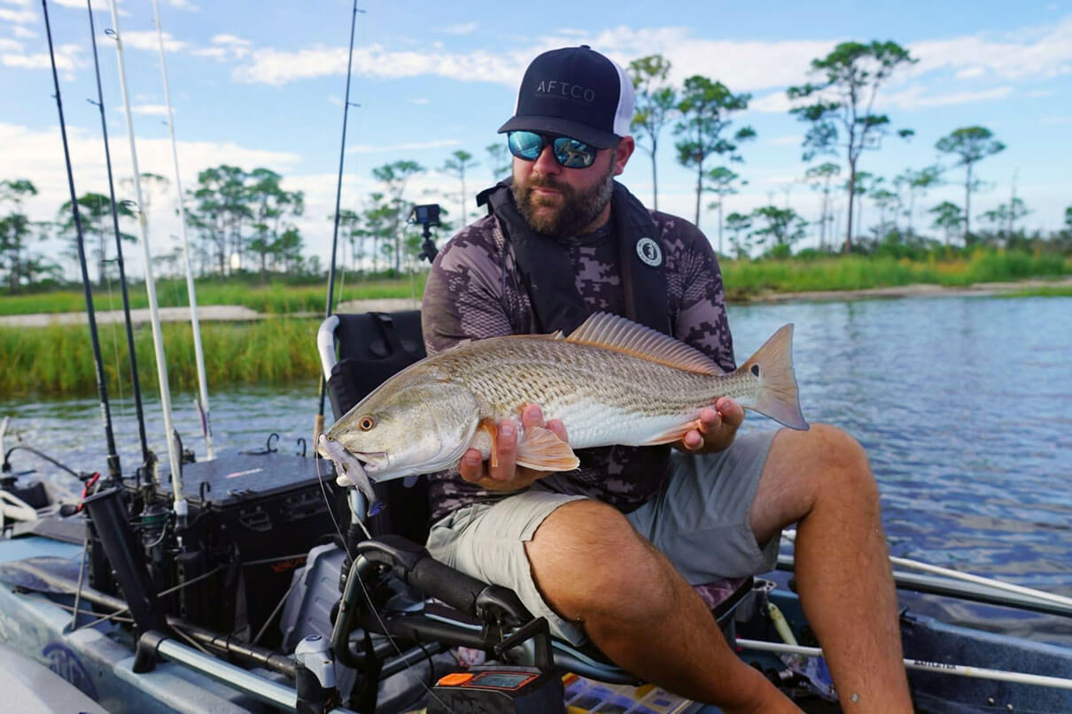 kayak angler holds up redfish caught while inshore fishing