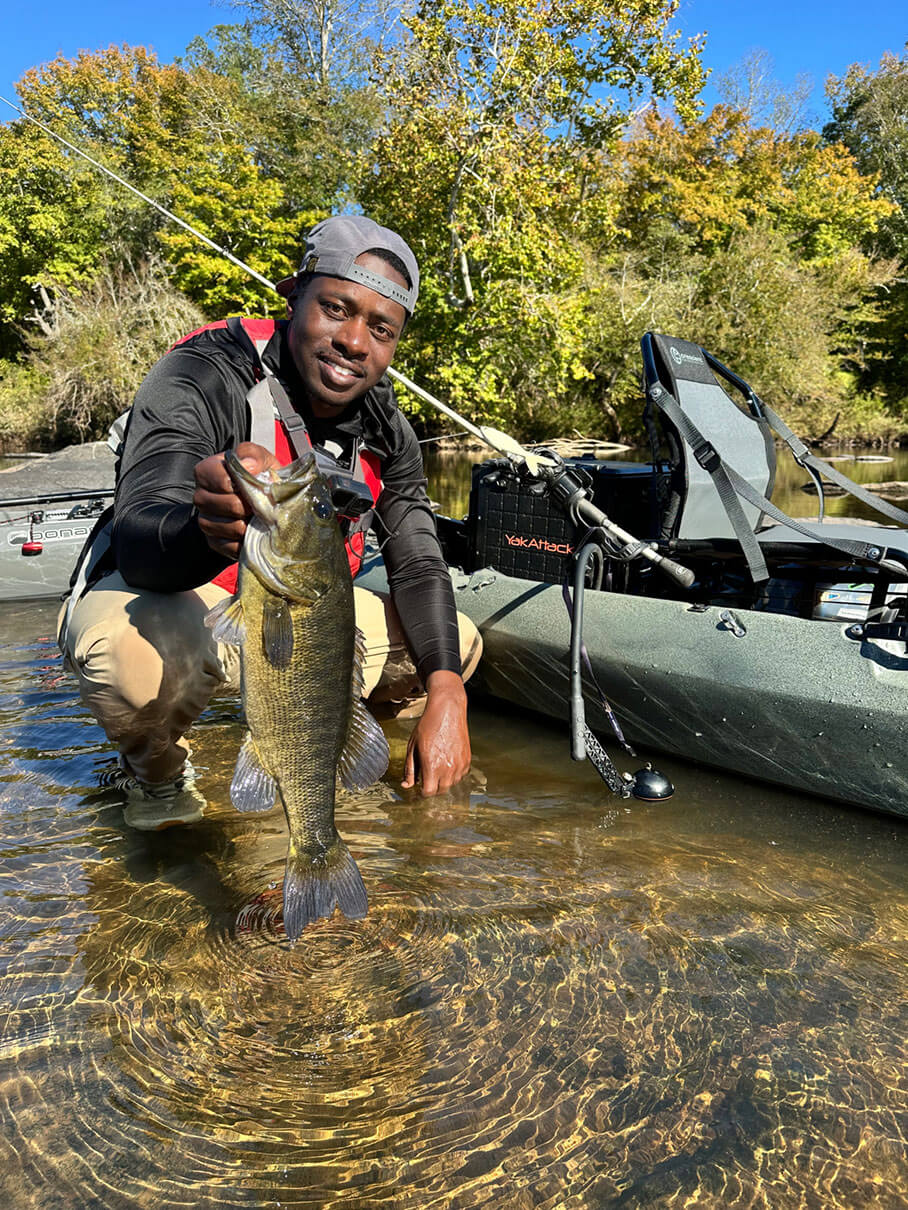 man holds up bass caught on while river fishing from a kayak