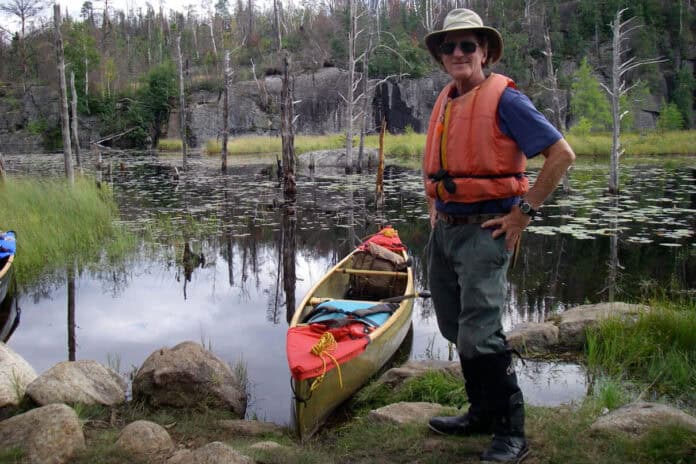 canoeist and symposium presenter Cliff Jacobson poses in the wilderness beside a tripping canoe