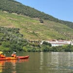 Join Our Upcoming Webinar On Kayak Expeditions In Portugal two people paddle an orange tandem kayak in front of terraced hills in the Douro river valley in Portugal