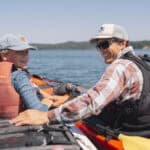Kayaking Washington’s San Juan Islands Is The Digital Detox Retreat Of The Summer A guide and young boy sit in kayaks side by side on the water surrounding the San Juan Islands.