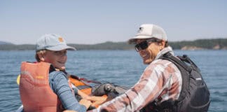Checking Sea Time In Washington’s San Juan Islands A guide and young boy sit in kayaks side by side on the water surrounding the San Juan Islands.