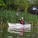 Kayak Review: BorealDesign’s Storm 17 man paddles the Boreal Design Storm 17 thermoformed touring kayak in front of cattails with a house in the background