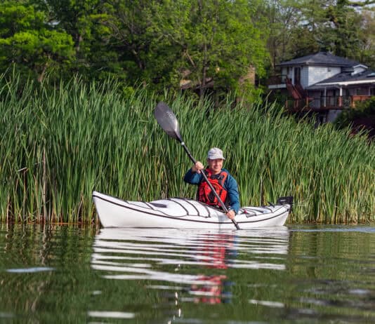 Kayak Review: BorealDesign’s Storm 17 man paddles the Boreal Design Storm 17 thermoformed touring kayak in front of cattails with a house in the background