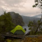 A Quick & Handy Guide to Repairing Waterproof Gear (Video) Image of a green tent with a rainfly on a tent platform in the rain