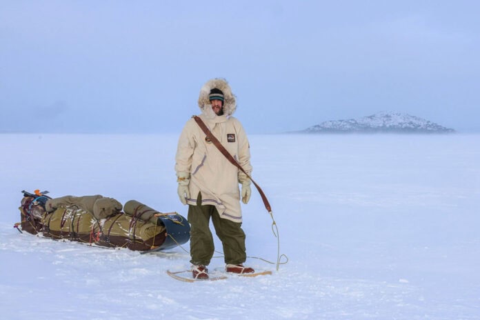 Justin Barbour stands in snowshoes and parka with his loaded sled in the tundra