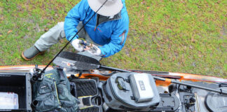 How To Create The Ultimate Fishing Kayak Setup angler crouches beside fishing kayak parked on grass while working on tackle setup
