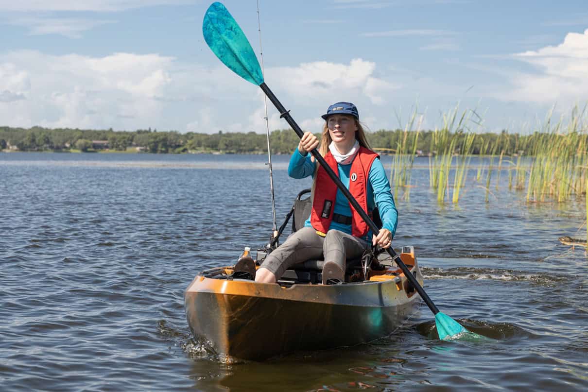 Woman paddling sit on top fishing kayak wearing yoke-style inflatable life jacket