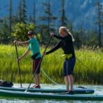 An Inflatable Life Jacket Could Save Your Life: Here’s How To Choose The Right One Two women on paddleboards wearing belt packs.