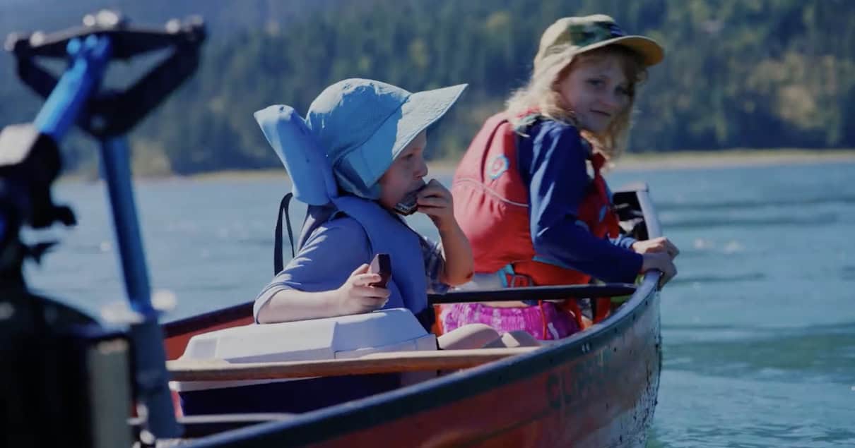 Two children seated in canoe eating snacks