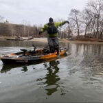 Beginners Guide To Kayak Fishing: Skills & Safety Kayak angler in a drysuit during cold weather tries jumping off his kayak into the water