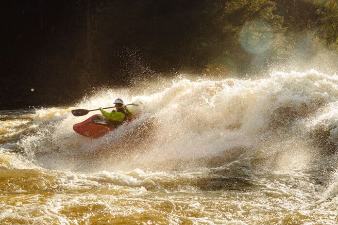 person whitewater kayaking through large rapids in golden light