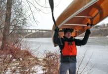 Frank Bures back at the scene of the capsize standing with canoe over his head in the wintertime