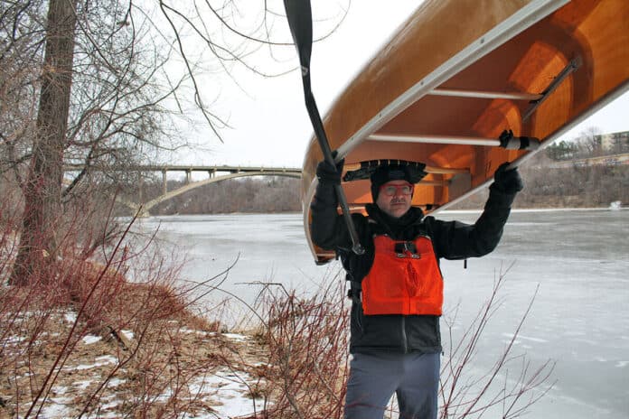 Frank Bures back at the scene of the capsize standing with canoe over his head in the wintertime