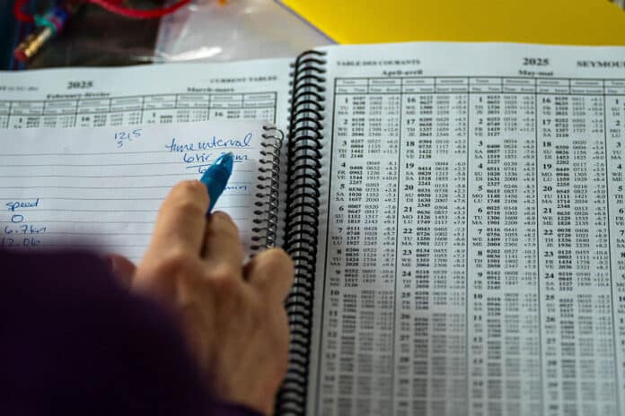 a person makes handwritten notes while scanning through a spiral bound tide table