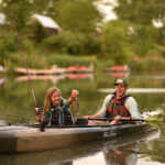 Get Started Kayak Fishing man sits in fishing kayak while young girl excitedly catches fish