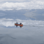 1,000 Miles to Tuk Two people in red canoe on lake like glass with mountains in background