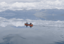 1,000 Miles to Tuk Two people in red canoe on lake like glass with mountains in background