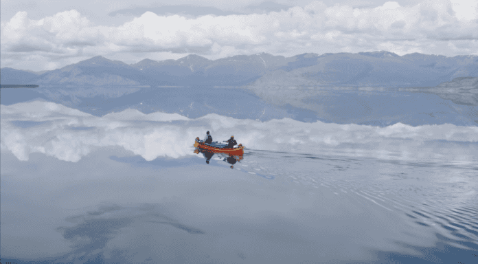 Two people in red canoe on lake like glass with mountains in background