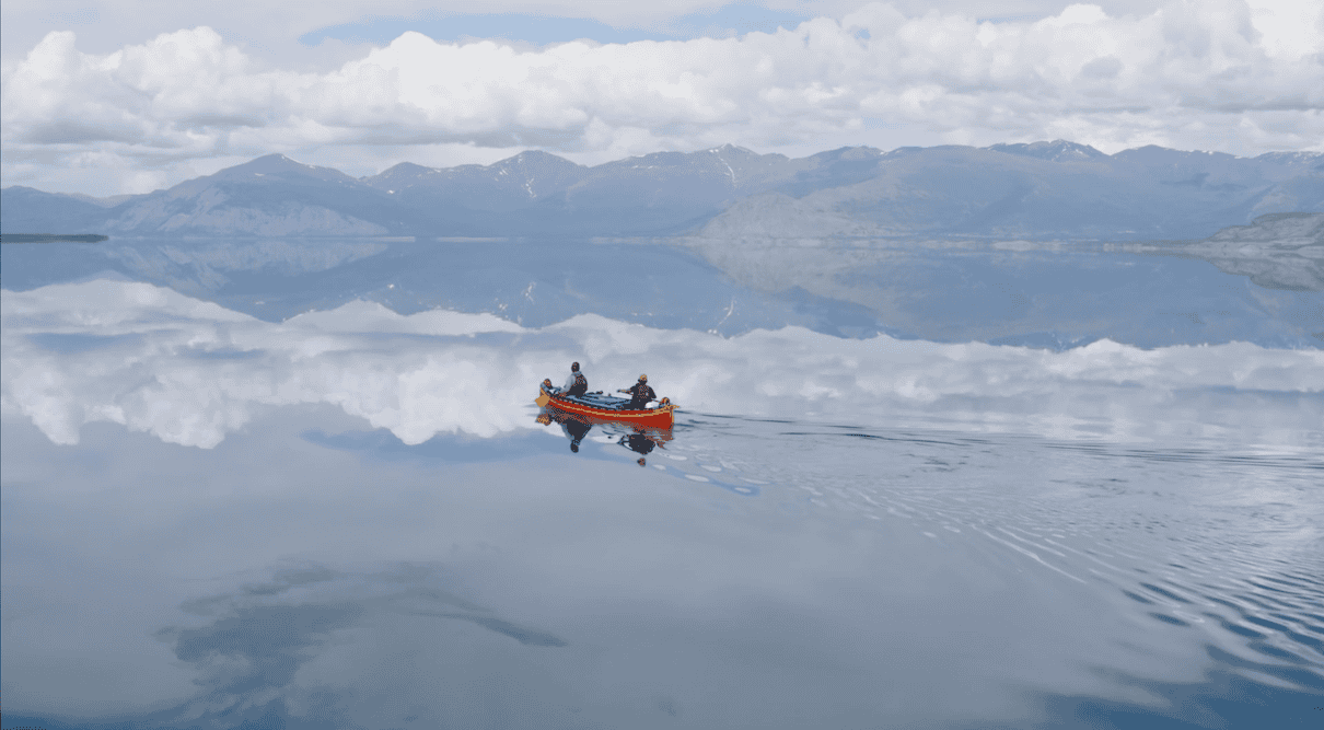 Two people in red canoe on lake like glass with mountains in background