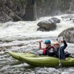 Whitewater Kayaking Hits the Big Screen in Apex Two women in green whitewater kayaks with rapids behind them