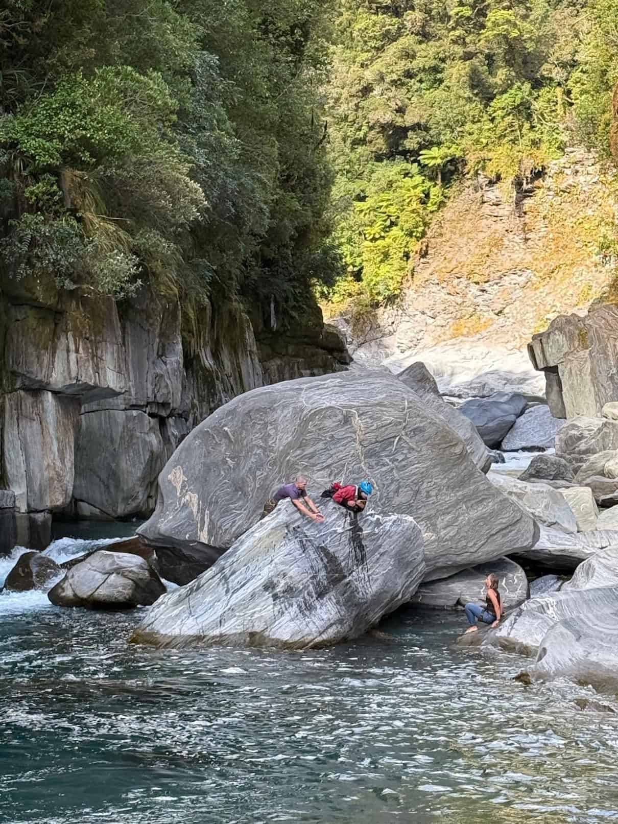 Two people on top of boulder looking down at person sitting on rock in middle of river