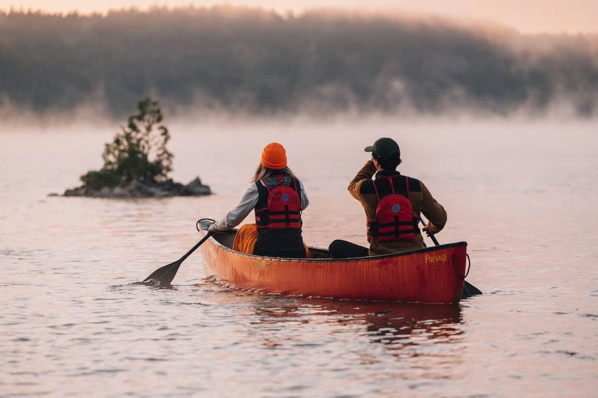 Two people paddling red canoe on misty lake