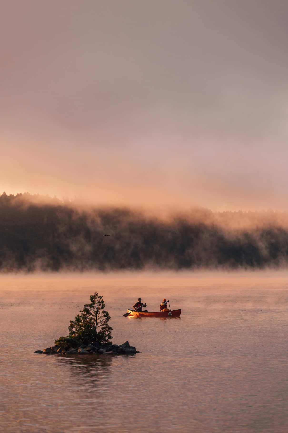 Two people in canoe paddling on misty lake