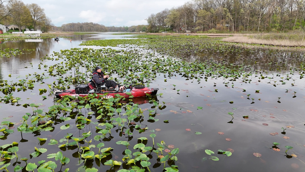 Man on fishing kayak fishing in lilypads on narrow lake
