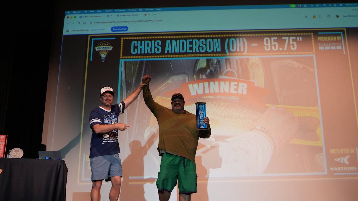 Two men on stage, one holding trophy and his other arm up