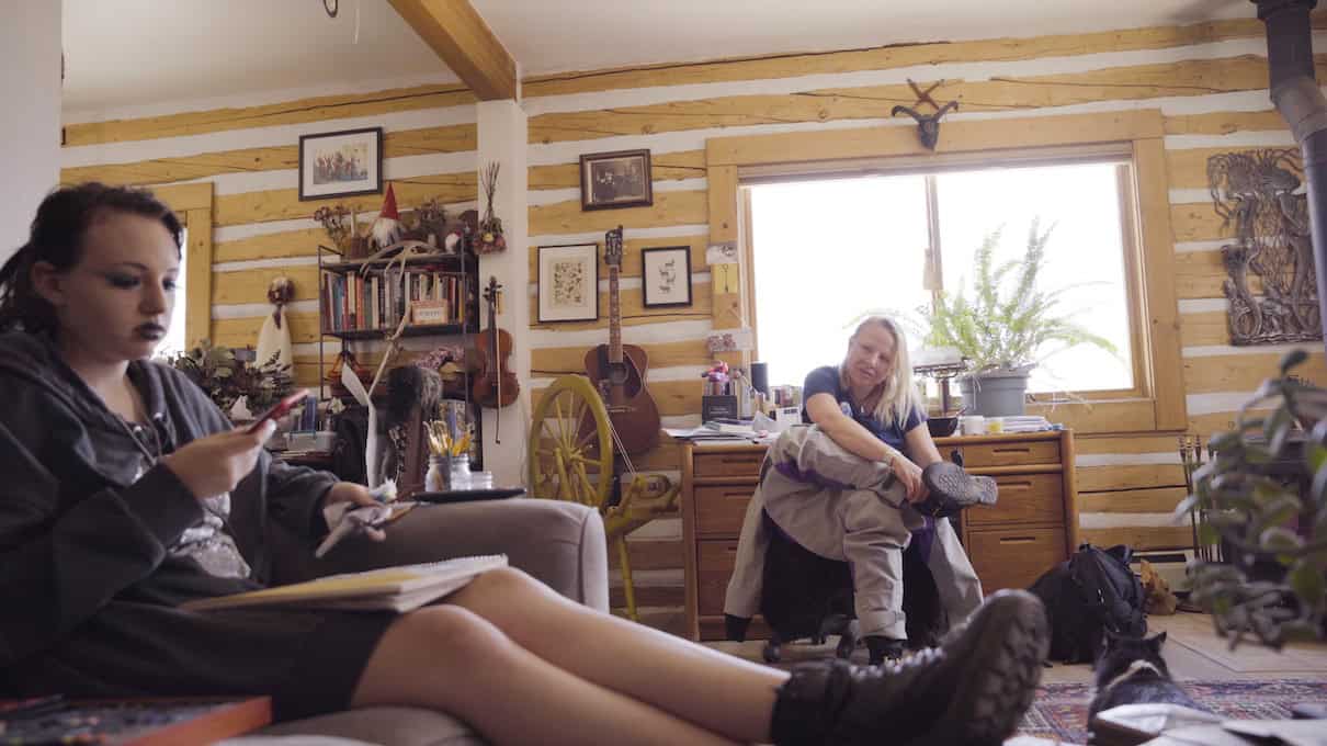 Elisha puts on her drysuit in the living room while Charlotte sits on couch