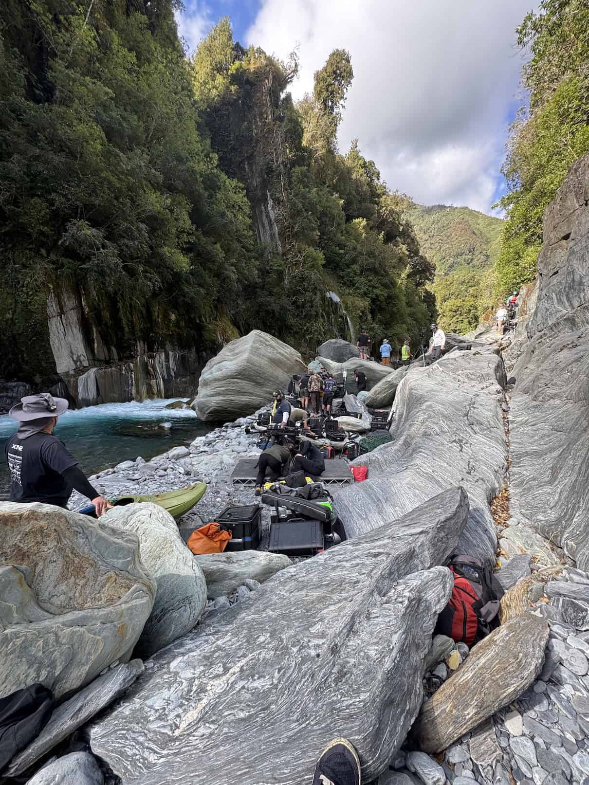 Film crew and equipment set up on rocky shore of river
